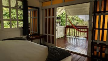 Quarto com cama, janela com vista para área verde e porta que dá para um espaço ao ar livre com uma rede.