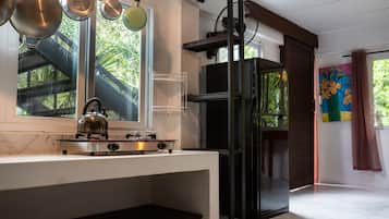 A kitchen with a gas stove, hanging pots, a window with a view of greenery, and a refrigerator.