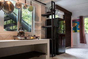 Una cocina con estufa a gas, ollas colgando, una ventana con vistas a la vegetación y un refrigerador.