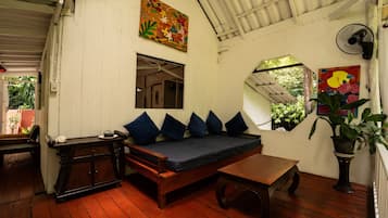 A room with a wooden bench, a sofa with cushions, a small table, and a fan.