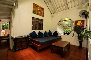 Una habitación con un banco de madera, un sofá con cojines, una mesita y un ventilador.