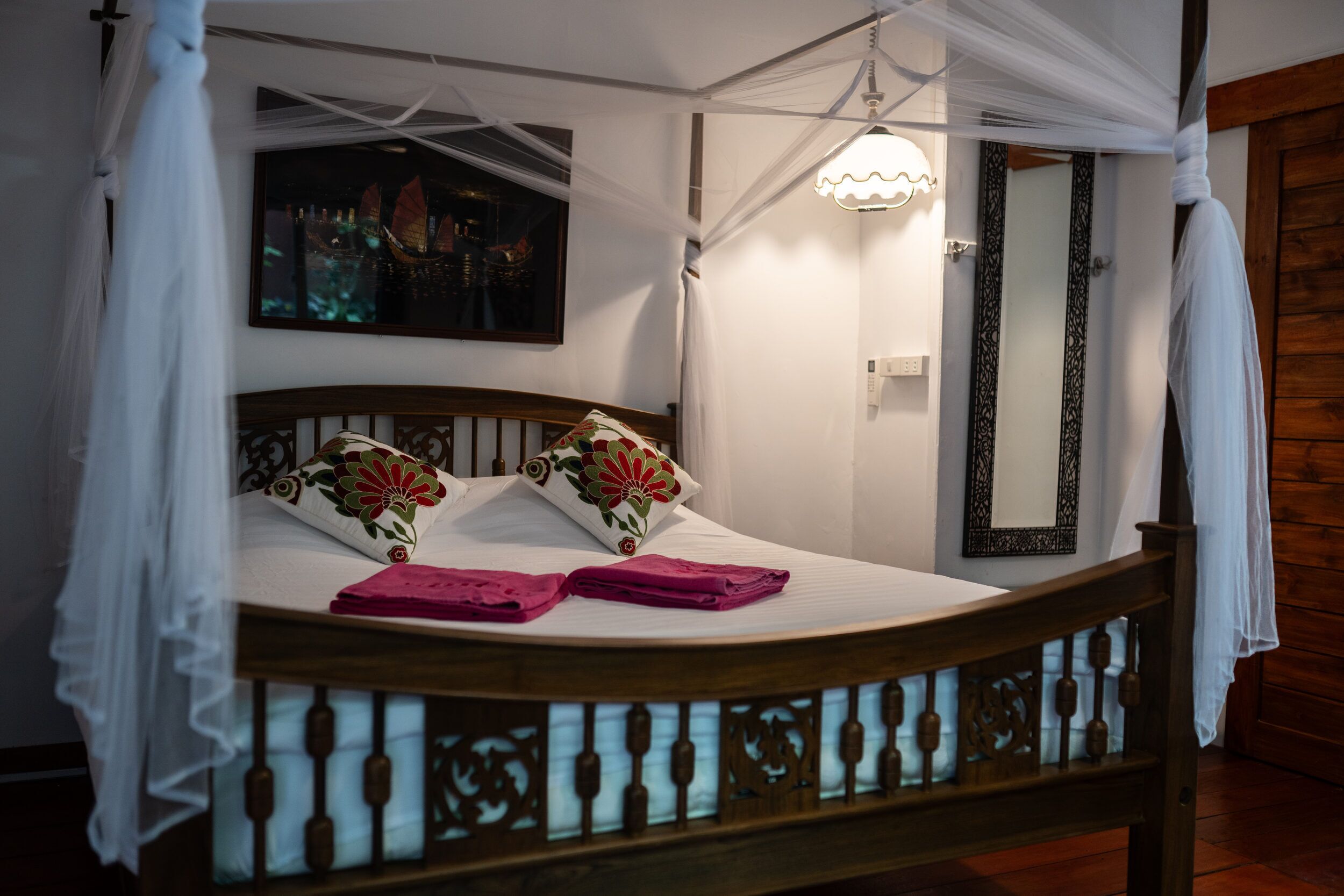 A bed with a canopy, a bedside lamp, a mirror, and a painting on the wall.