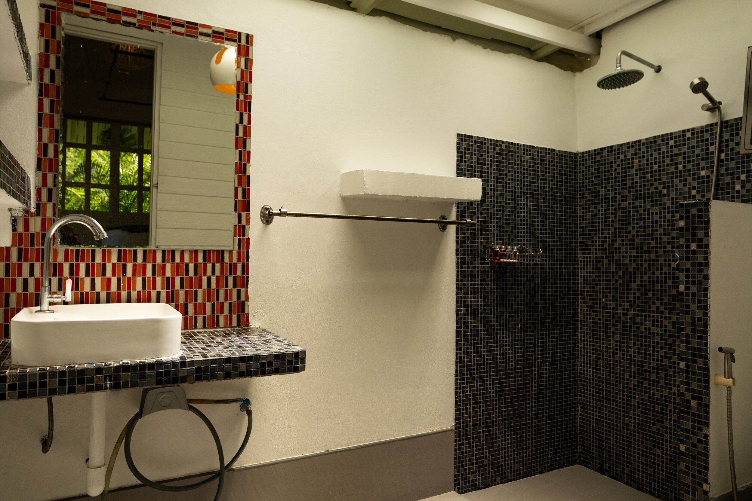 A bathroom with a white sink, a mirror, a shower with a black tiled wall, and a towel rack.