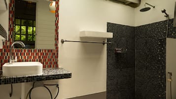 A bathroom with a white sink, a mirror, a shower with a black tiled wall, and a towel rack.