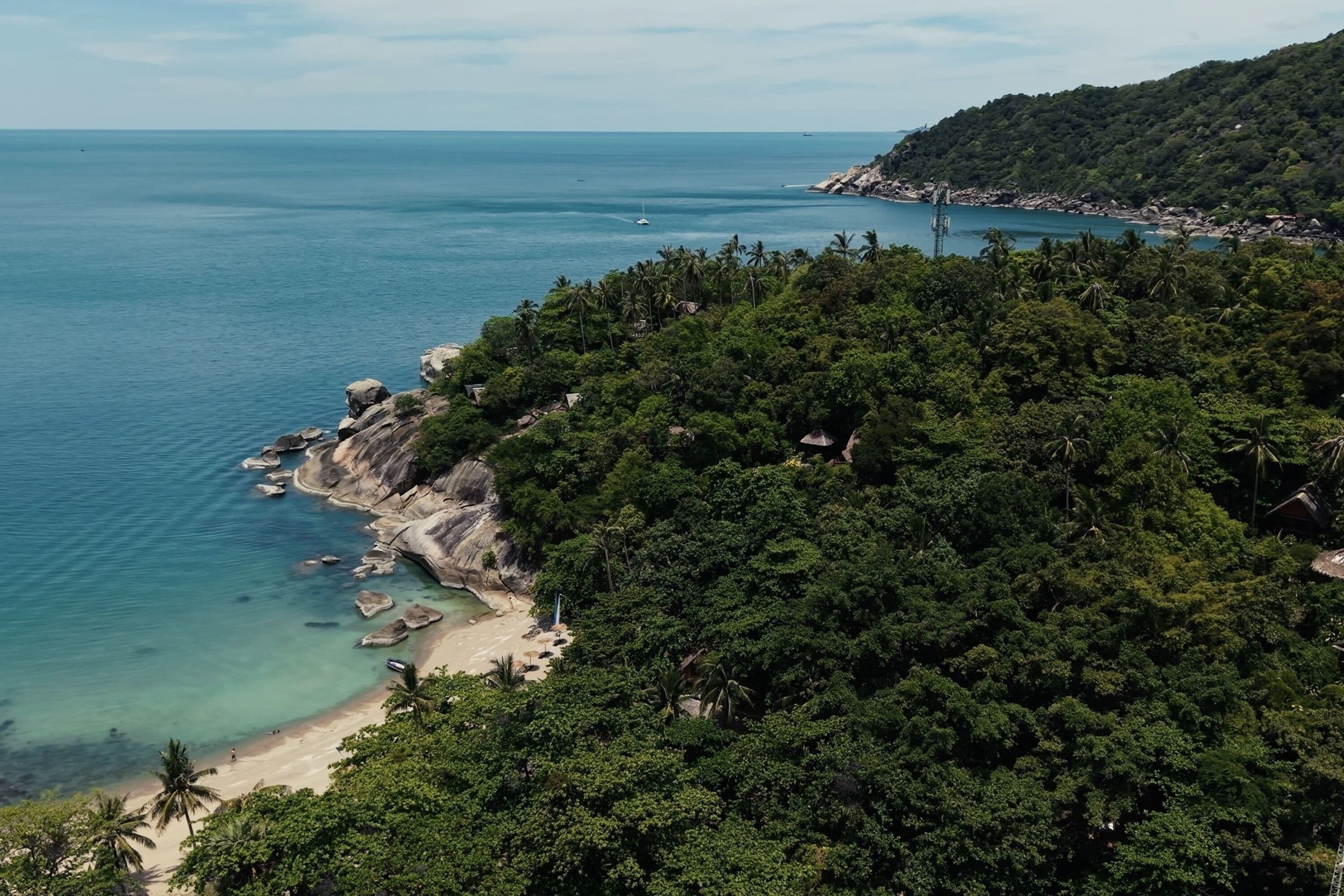 Paisagem costeira com uma praia, vegetação densa e uma vista clara do mar.