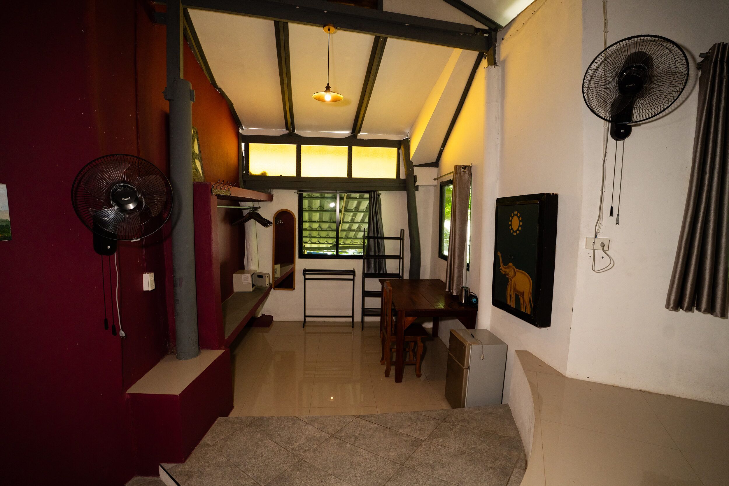 A room with a dining area, a standing fan, a window with curtains, and a painting on the wall.