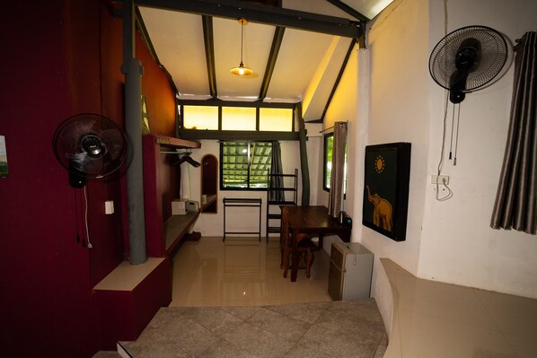 A room with a dining area, a standing fan, a window with curtains, and a painting on the wall.