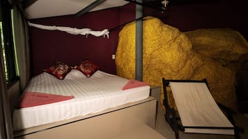 A bed with a white mattress and red pillows, a small bedside table, and a large golden sculpture.