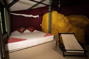Una cama con colchón blanco y almohadas rojas, una mesita de noche pequeña y una escultura dorada grande.