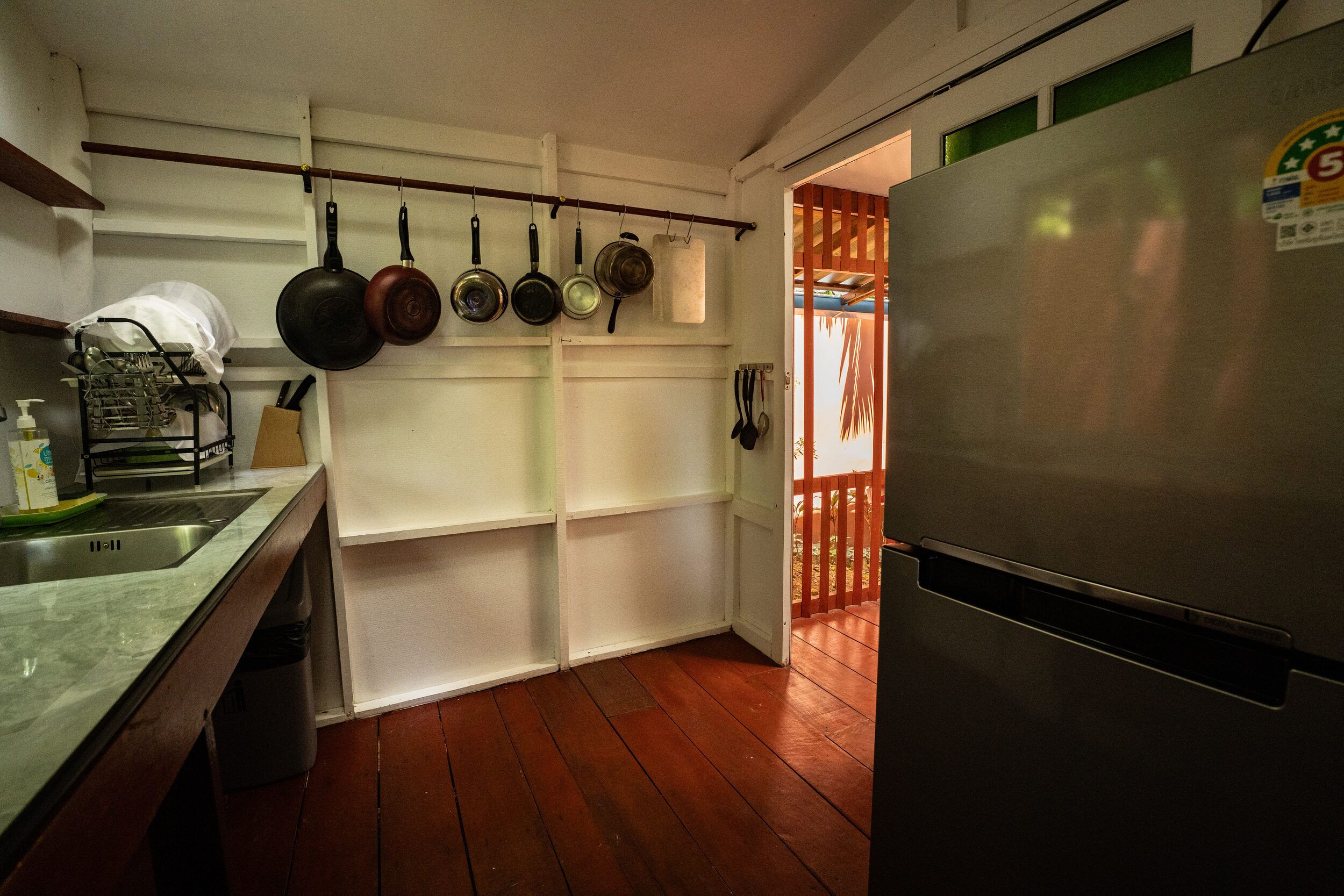 A kitchen with a stainless steel refrigerator, wooden flooring, and a dish rack with utensils.