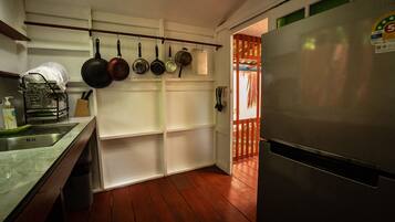 A kitchen with a stainless steel refrigerator, wooden flooring, and a dish rack with utensils.