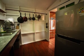 Una cocina con refrigerador de acero inoxidable, piso de madera y un escurreplatos con utensilios.