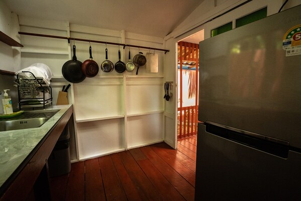 Una cocina con refrigerador de acero inoxidable, piso de madera y un escurreplatos con utensilios.