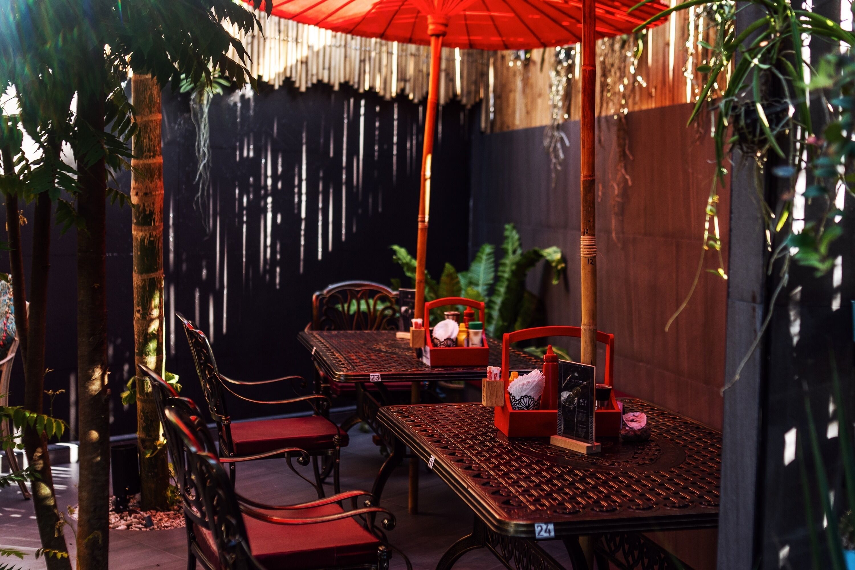 An outdoor dining area with a table and chairs, a red umbrella, and a bamboo pole.