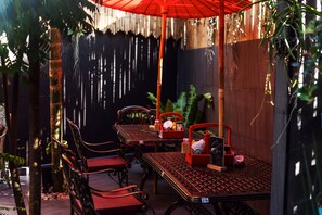 An outdoor dining area with a table and chairs, a red umbrella, and a bamboo pole.