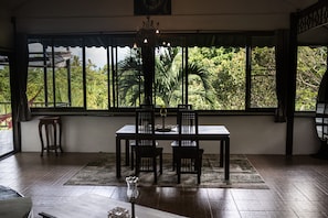 A dining area with a table and chairs, large windows with a view of greenery, and a chandelier.