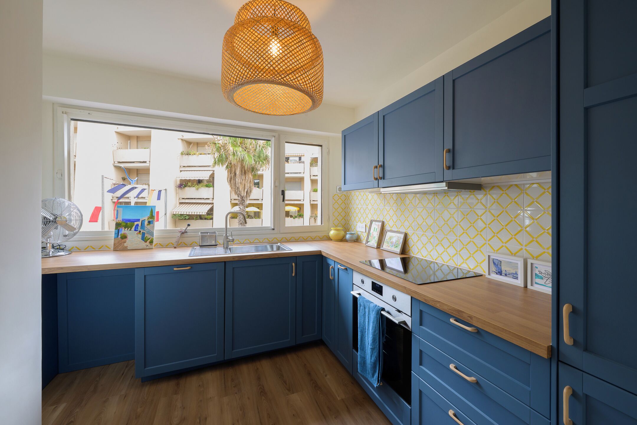 Una cucina moderna con mobili blu, un piano di lavoro in legno e un'ampia finestra che si affaccia su un balcone.