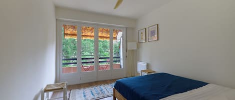 Une chambre à coucher comprenant un lit, un ventilateur de plafond, une fenêtre avec vue et une porte donnant sur un espace extérieur.