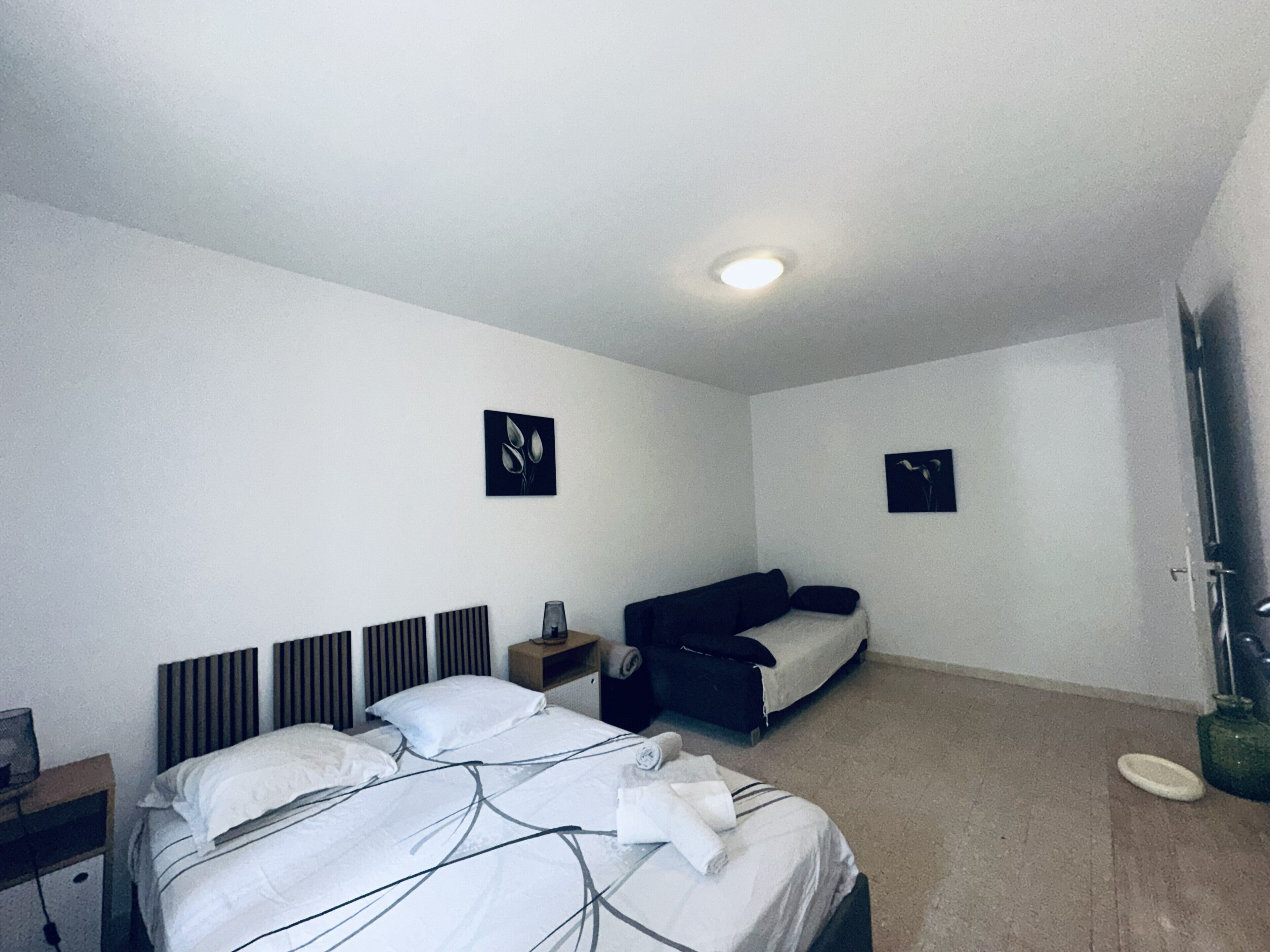 A hotel room with a bed, a sofa, a small table, and two wall-mounted artworks.