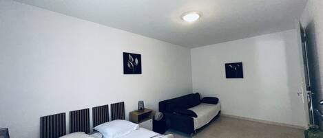 A hotel room with a bed, a sofa, a small table, and two wall-mounted artworks.
