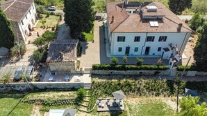 A large building with a tiled roof, a stone wall, and a grassy area with outdoor furniture. - Le Mortinete Farmstay: Colombino (Toscana)