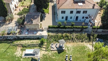 A large building with a tiled roof, a stone wall, and a grassy area with outdoor furniture.