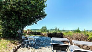 An outdoor seating area with stone flooring, metal chairs, and a table with a bowl of fruit. - Le Mortinete Farmstay: Colombino (Toscana)