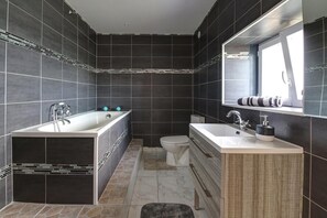 Une salle de bain moderne avec une baignoire sur pieds, des toilettes séparées et un meuble-lavabo avec un miroir.