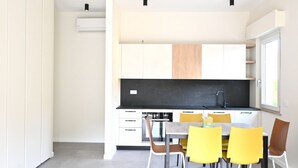 Una cocina moderna con armarios blancos, encimera negra y un comedor con sillas amarillas.