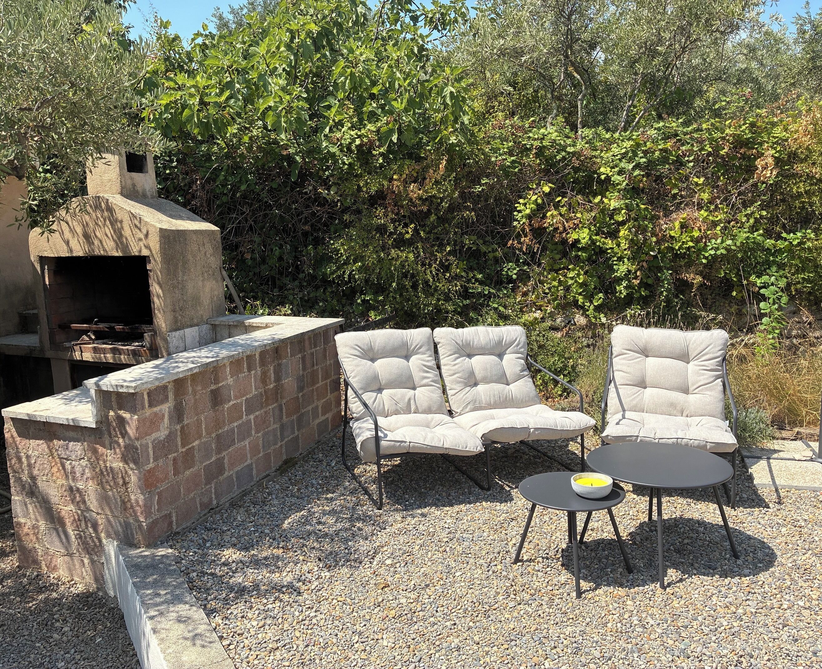 An outdoor seating area with a stone-built barbecue grill, two cushioned chairs, and a small round table with a candle.