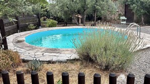 Une piscine ronde bordée de pierres, entourée d’une clôture en bois et agrémentée de différentes plantes.