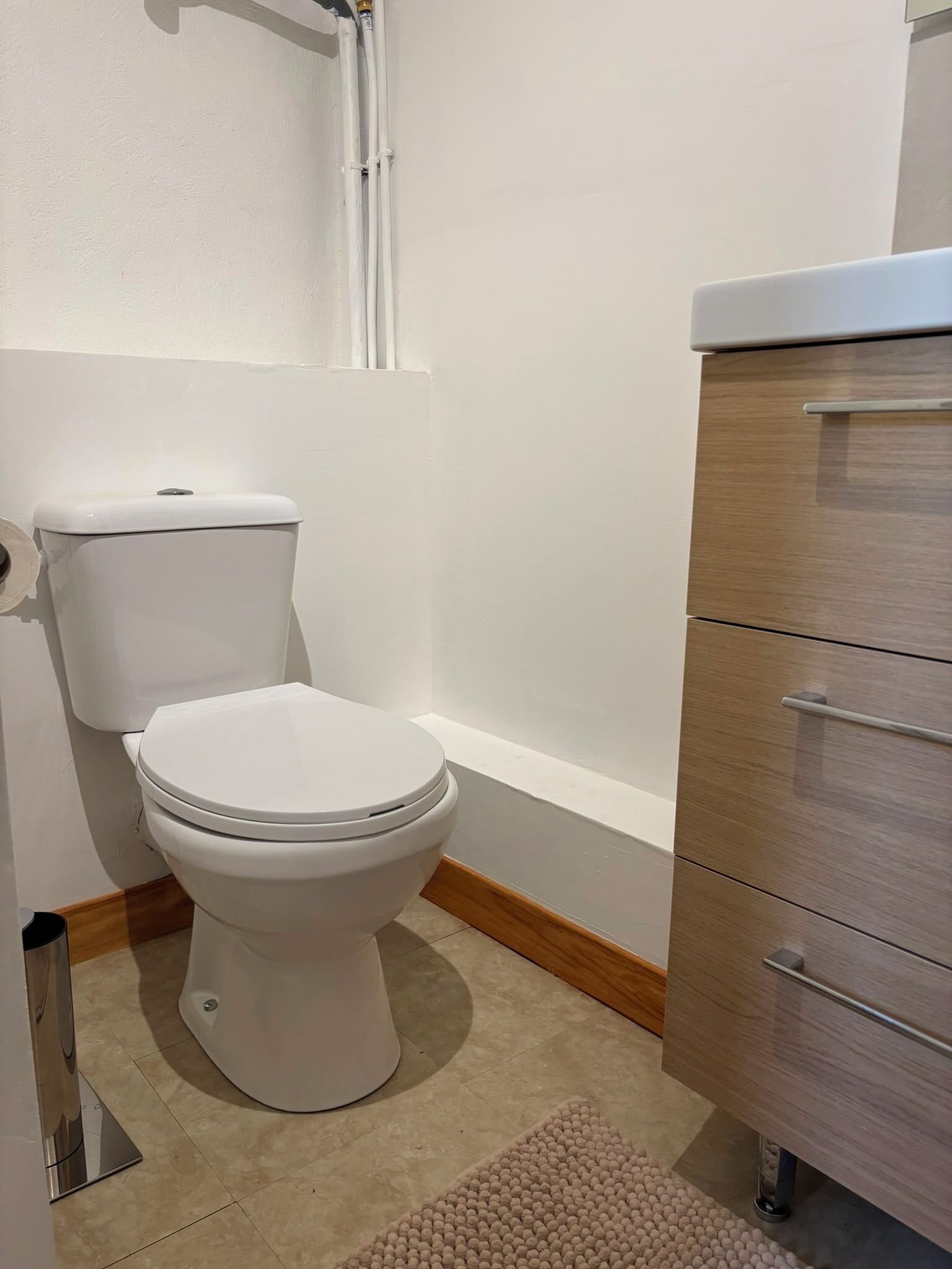 A bathroom with a toilet, a wooden cabinet, and a bathtub.