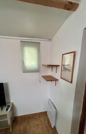Ein kleiner Raum mit Fenster, Heizkörper, TV-Standfuß und zwei Holzregalen.