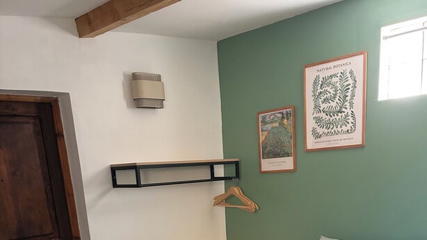 Une chambre à coucher avec un lit, une table de chevet avec une lampe, une porte en bois et deux reproductions botaniques encadrées accrochées au mur.