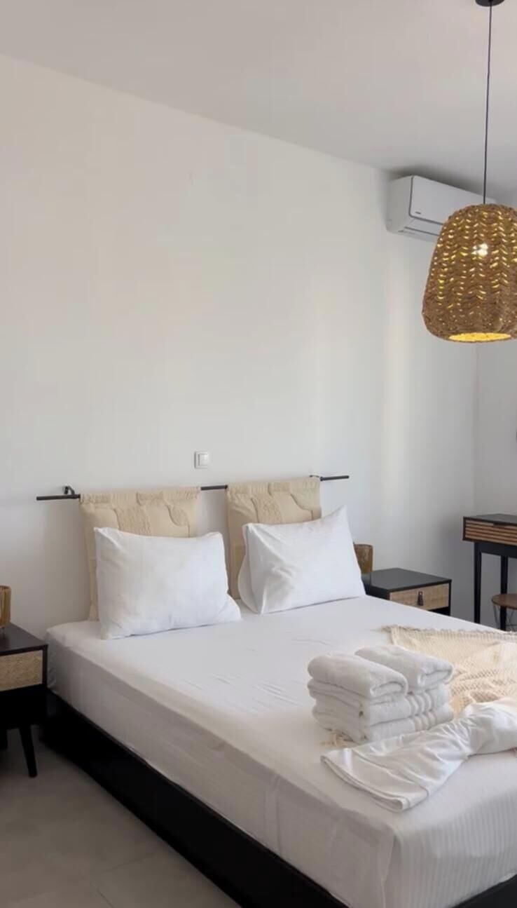 Een slaapkamer met een bed, twee nachtkastjes, een hanglamp en een wandairconditioning.