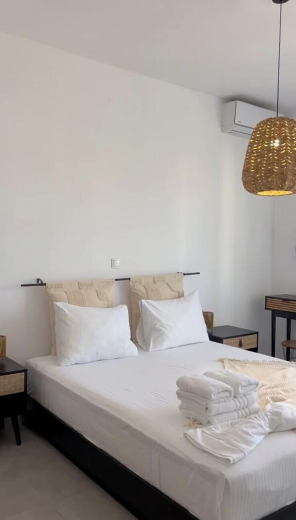Une chambre à coucher comprenant un lit, deux tables de chevet, un luminaire suspendu et un appareil de climatisation fixé au mur.