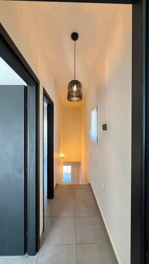 Un couloir avec un luminaire suspendu, une porte sur la gauche et une fenêtre au fond.