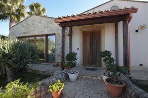Ein Haus mit einer Steinfassade, einer Holzpergola und Kübelpflanzen.