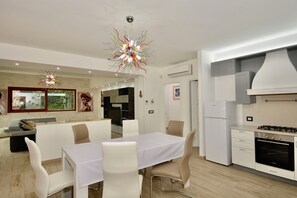 Eine moderne Küche mit weißen Schränken, ein Essbereich mit weißem Tisch und Stühlen sowie ein besonderer Kronleuchter.
