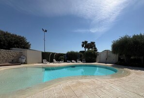 Ein Pool mit Liegestühlen, einer Steinmauer und einer Palme.