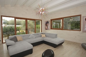 Ein modernes Wohnzimmer mit einer Eckcouch, großen Fenstern und einem außergewöhnlichen Kronleuchter.