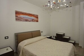 Ein Schlafzimmer mit einem Bett, einem Nachttisch, einer Stehlampe, einer modernen Chandelier und einem Bild an der Wand.