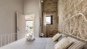 Ein Schlafzimmer mit Steinwand, einem Bett mit Metallkopfteil, einem Sessel und einem kleinen Tisch.