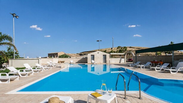 Ein Poolbereich mit Liegestühlen und einem kleinen Gebäude, vermutlich eine Poolbar oder Umkleidekabine.