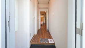 Un pasillo con piso de madera, paredes blancas y una puerta a la izquierda.