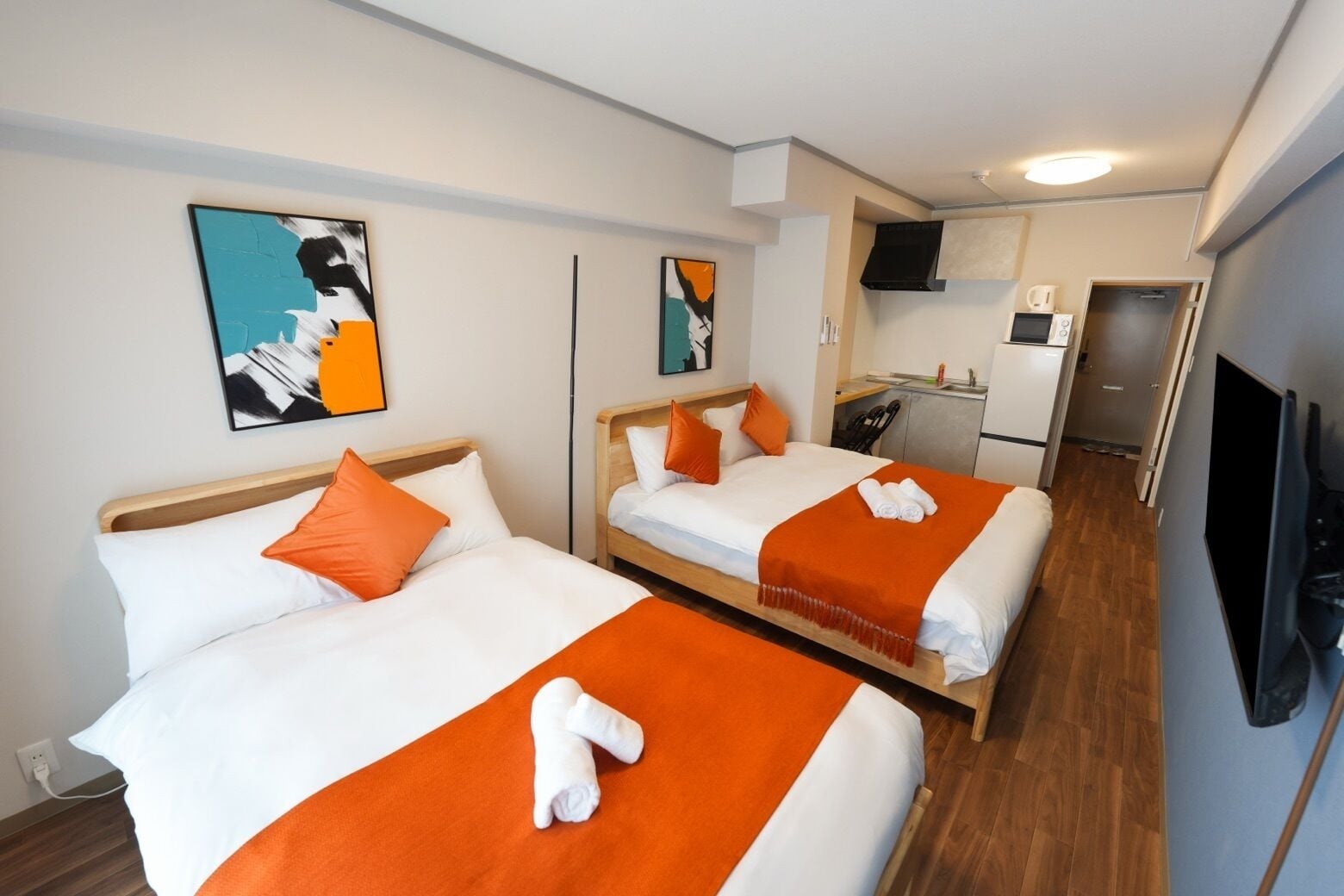 A hotel room with two beds, a kitchenette, and a television.