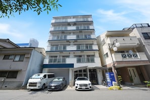 A multi-story residential building with a garage, parked cars, and a clear sky. - Stay Link Japan (Ichioka-Motomachi Minato-ku Osaka City)