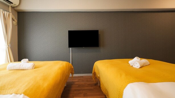 Habitación de hotel con dos camas, un televisor de pantalla plana en la pared y piso de madera.