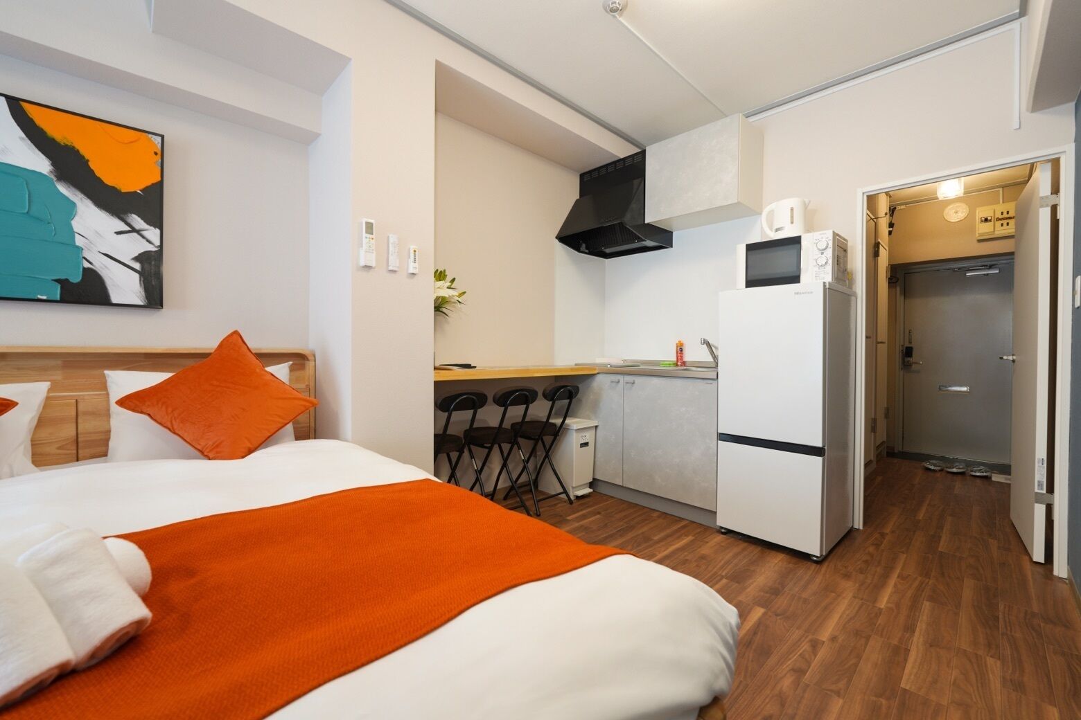 A compact hotel room with a bed, a kitchenette, and a bathroom.