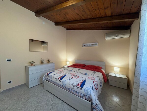 Ein Schlafzimmer mit einem Bett, Nachttischen, einer Kommode, einem Spiegel, einer Klimaanlage und einem Fenster mit Vorhängen.